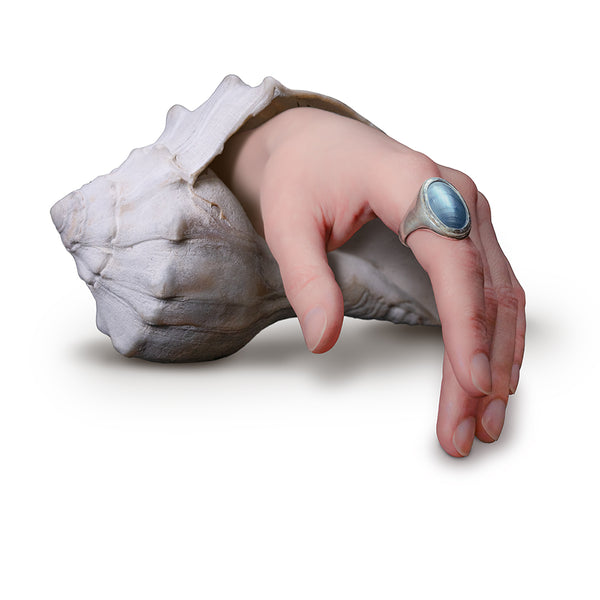 Hand emerging from a shell with a blue gemstone ring on a white background