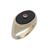 An angled shot of a gold ring with oval black onyx stone set with round ruby in the center.
