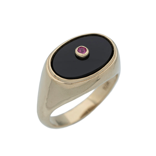 An angled shot of a gold ring with oval black onyx stone set with round ruby in the center.

