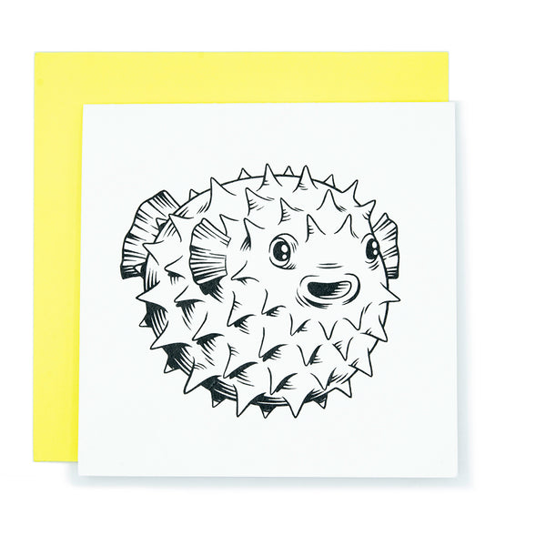 A square white card with an ink drawing of a pufferfish.  The card is resting on a bright yellow envelope.