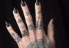 A tattoed hand with black fingernails wearing a large and small silver ship ring.
