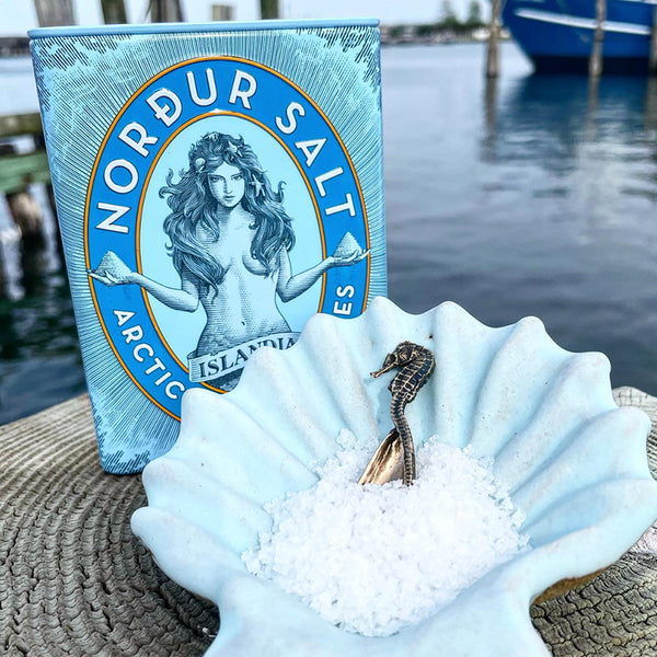 blue nordur salt tin with salt in shell in front of water background