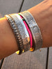 A group of silver nautical cuff bracelets on the wrist of a model.  There is a hot pink shell bracelet in the middle of the 3 silver bracelets.