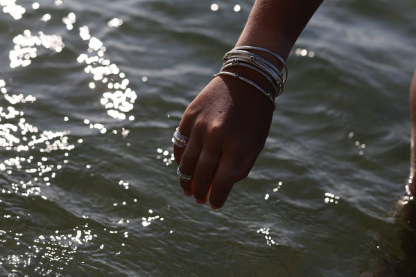 A model shot of  tan arm with silver bracelets and rings.  The arm is over ocean water.
