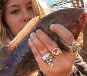 girl holding fish wearing rings, a skull ring a whale cameo ring and a ship ring
