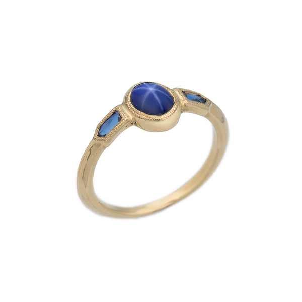 A gold ring with star sapphire pointing up and two bullet shaped sapphires on sides.