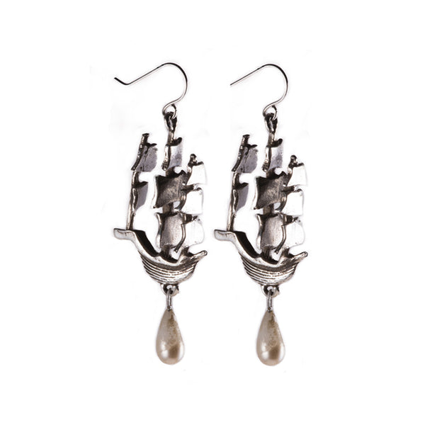 A pair of polished silver earrings in the shape of ships with tear drop shaped pearls hanging from the ships hull.