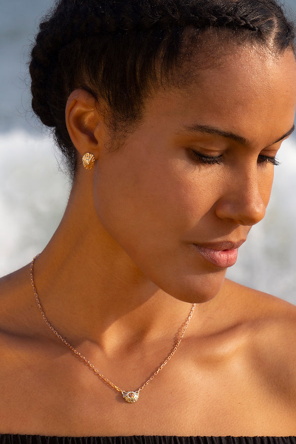A model wearing rose gold limpet shell earrings and a silver and rose gold barnacle necklace.  Her hair is braided and she is looking down.