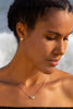 A model wearing rose gold limpet shell earrings and a silver and rose gold barnacle necklace.  Her hair is braided and she is looking down.