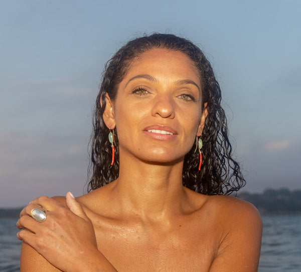 A model with her hand over her shoulder and wet hair wearing aquamarine stone and red coral earrings.
