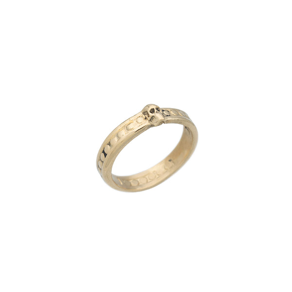 An Angled view of  gold band ring with small raised skull and beaded detail.