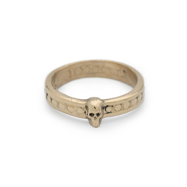A gold band ring with small raised skull and beaded detail.