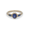 A gold ring with oval star sapphire in center and two bullet sapphires on sides with millgrain detail.